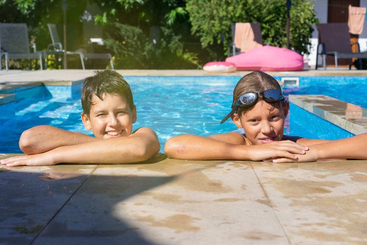 Two children in long-sleeve swim shirts running at the water's edge