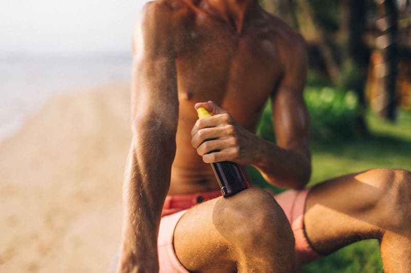 Spray sunscreen being applied to a leg on a sunlit beach